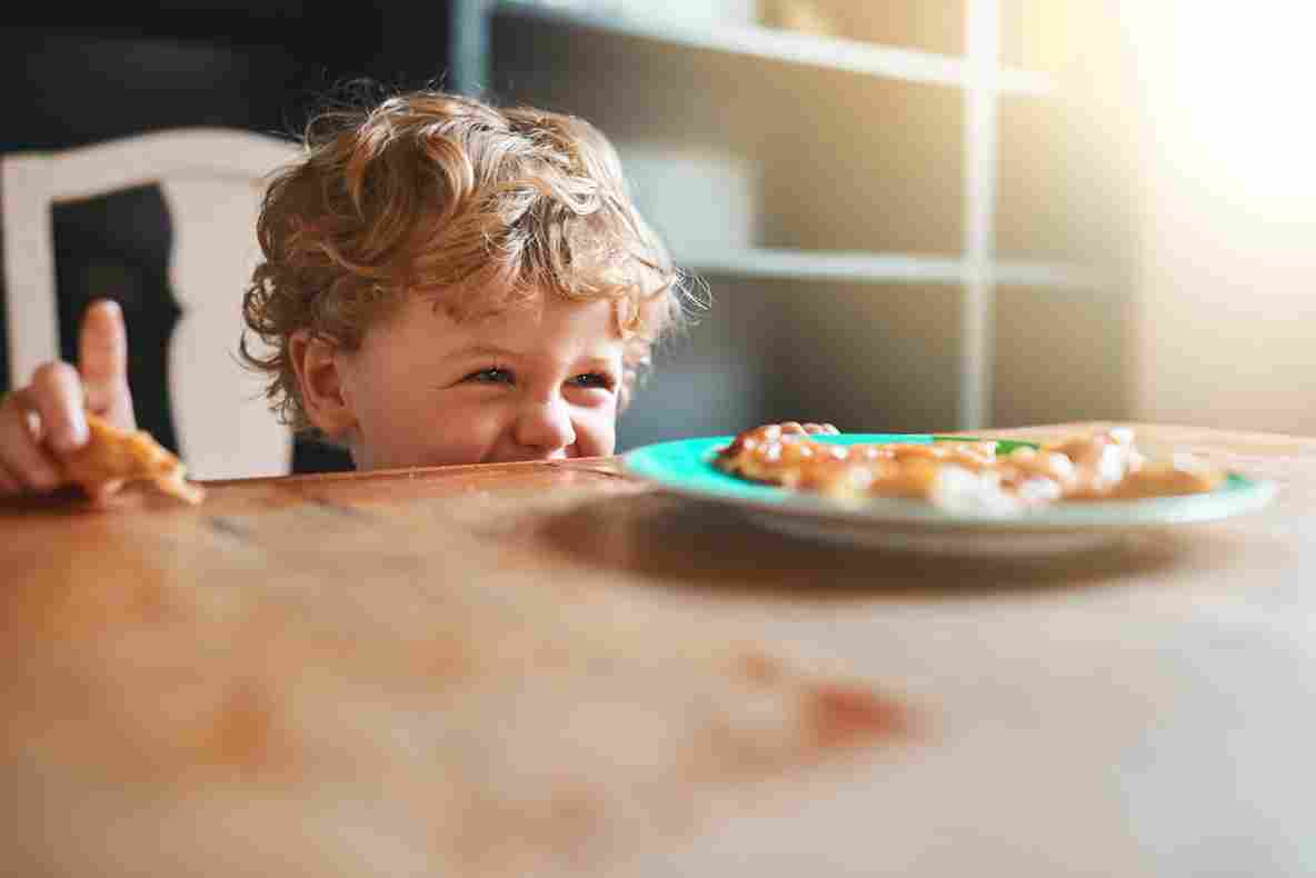 Malo dete proviruje preko stola i gleda u tanjir sa hranom