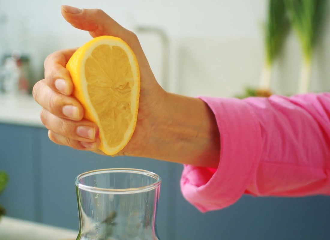 ženska osoba cedi limun u staklenu flašu sa vodom