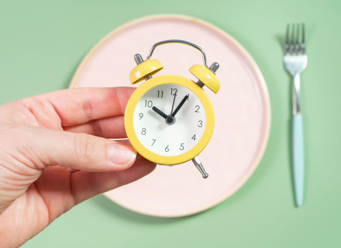 prikaz osobe koja drži sat u ruci, tanjira i viljuške pored simulirajući na fasting dijetu