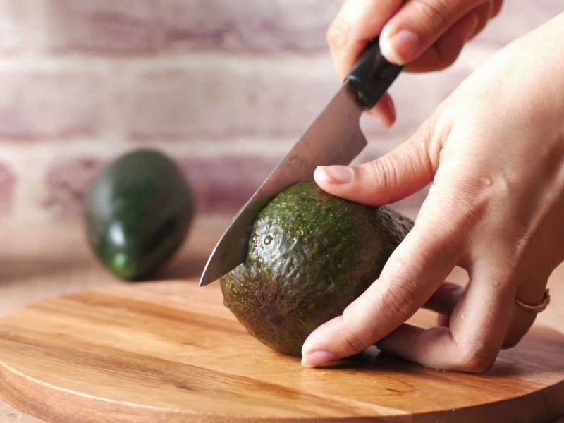 osoba seče avokado na drvenoj dasci