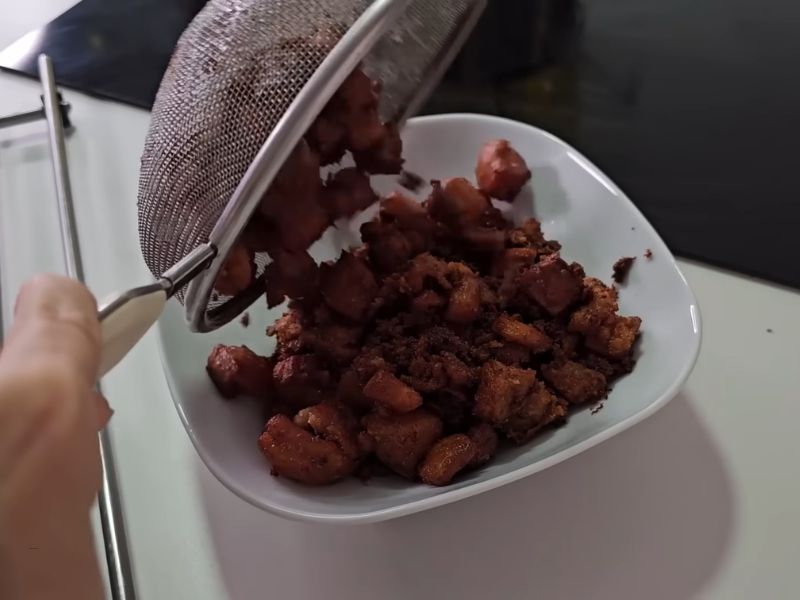 osoba proceđuje čvarke uz pomoć sita