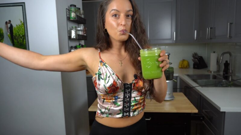 Žena pije zeleni sok u kuhinji kao deo jednodnevnog detoksa organizma
