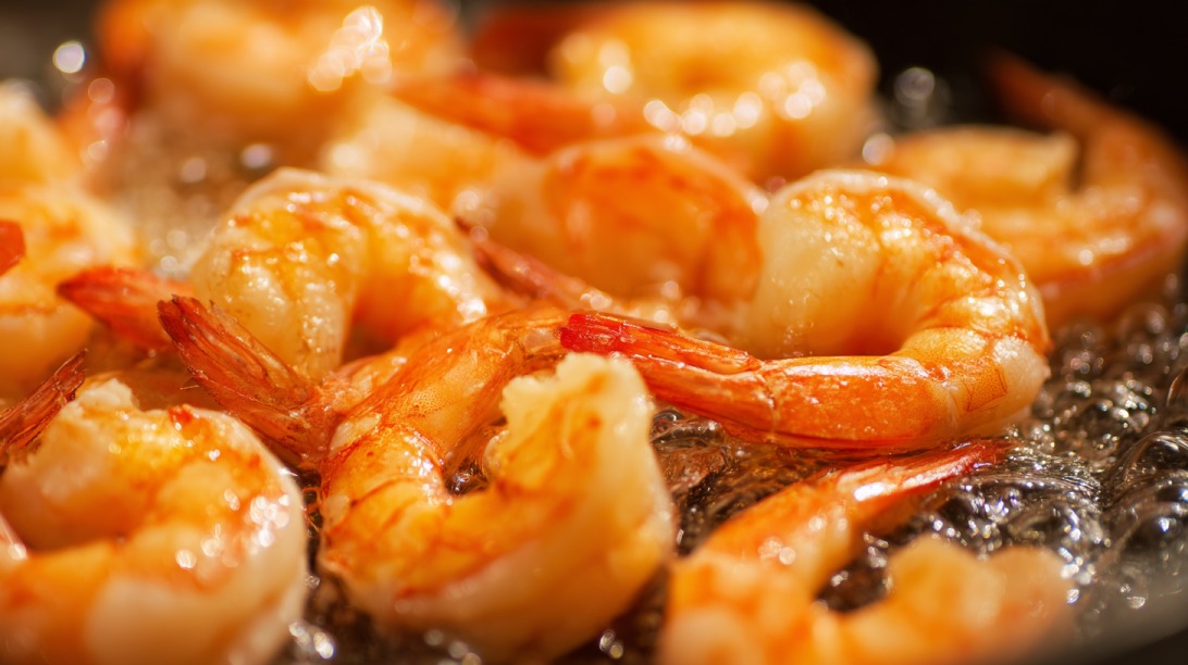 Close up of peeled shrimp cooking in bubbling oil in a pan