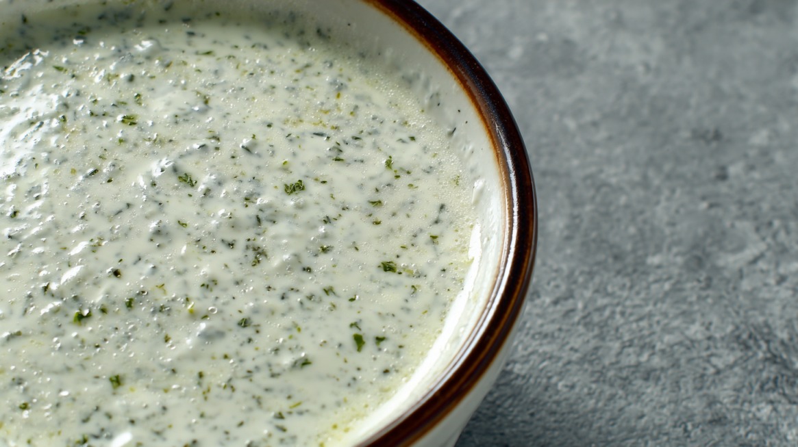 Close up of a bowl filled with white ranch dressing speckled with green herbs