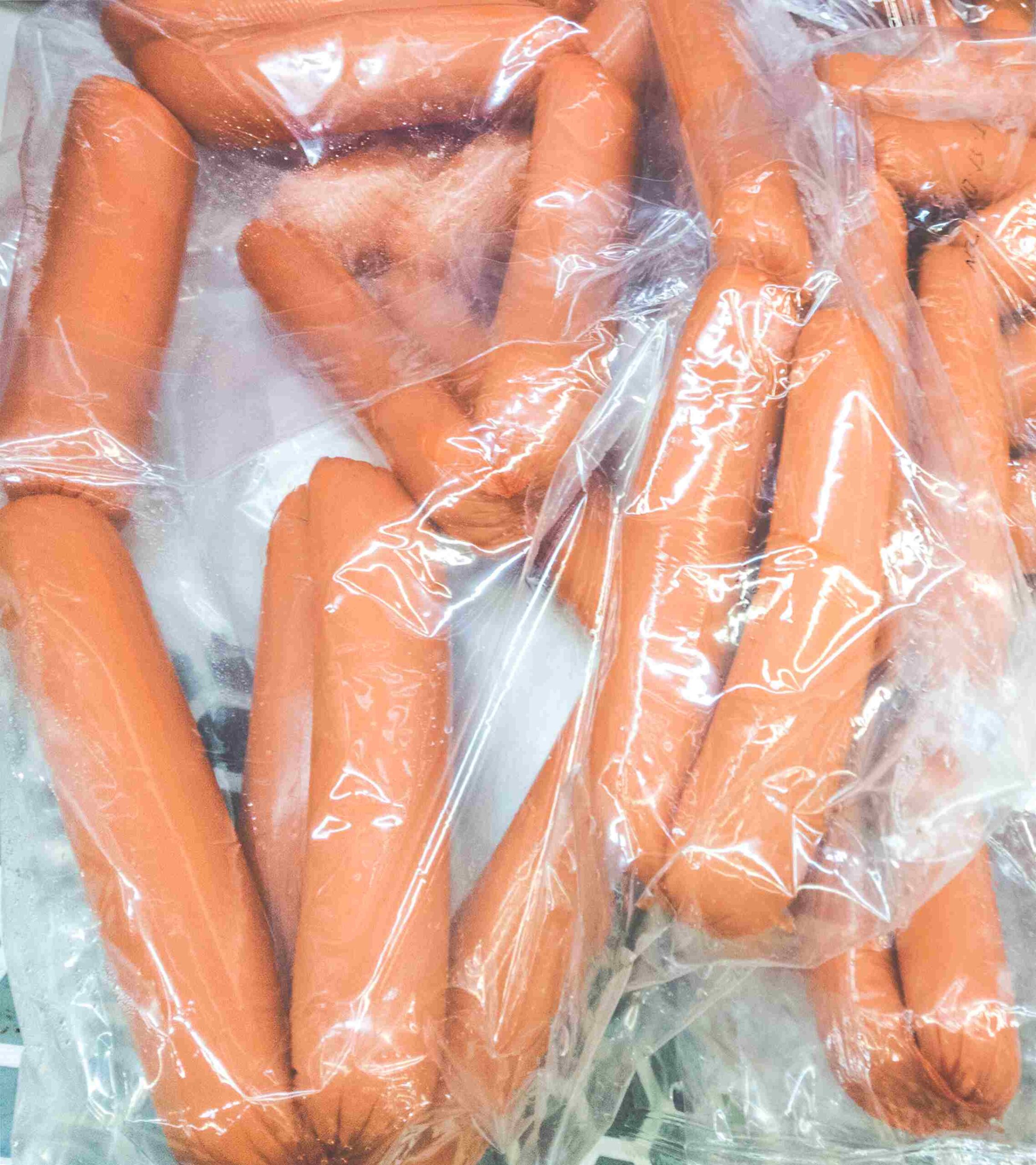 Hot dogs sealed in clear plastic bags with visible ice crystals in a freezer