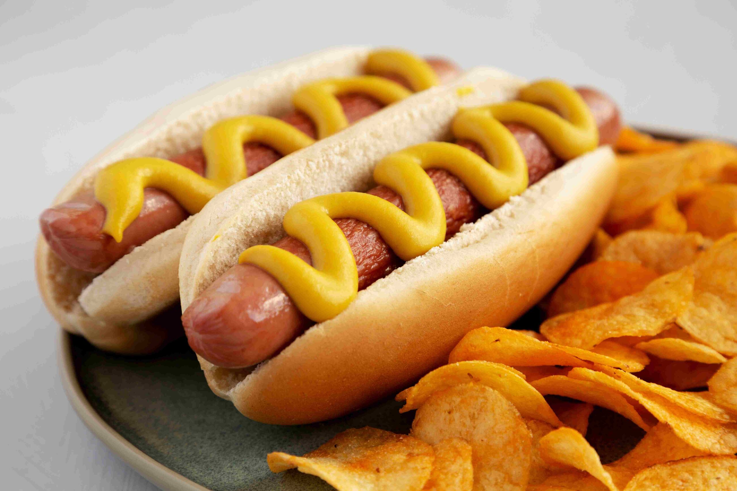 Two hot dogs topped with mustard served with potato chips on a plate