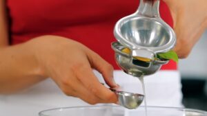 A person squeezing fresh lemon juice into a small measuring cup using a handheld citrus press
