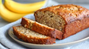 Sliced banana oat bread on a plate with bananas in the background