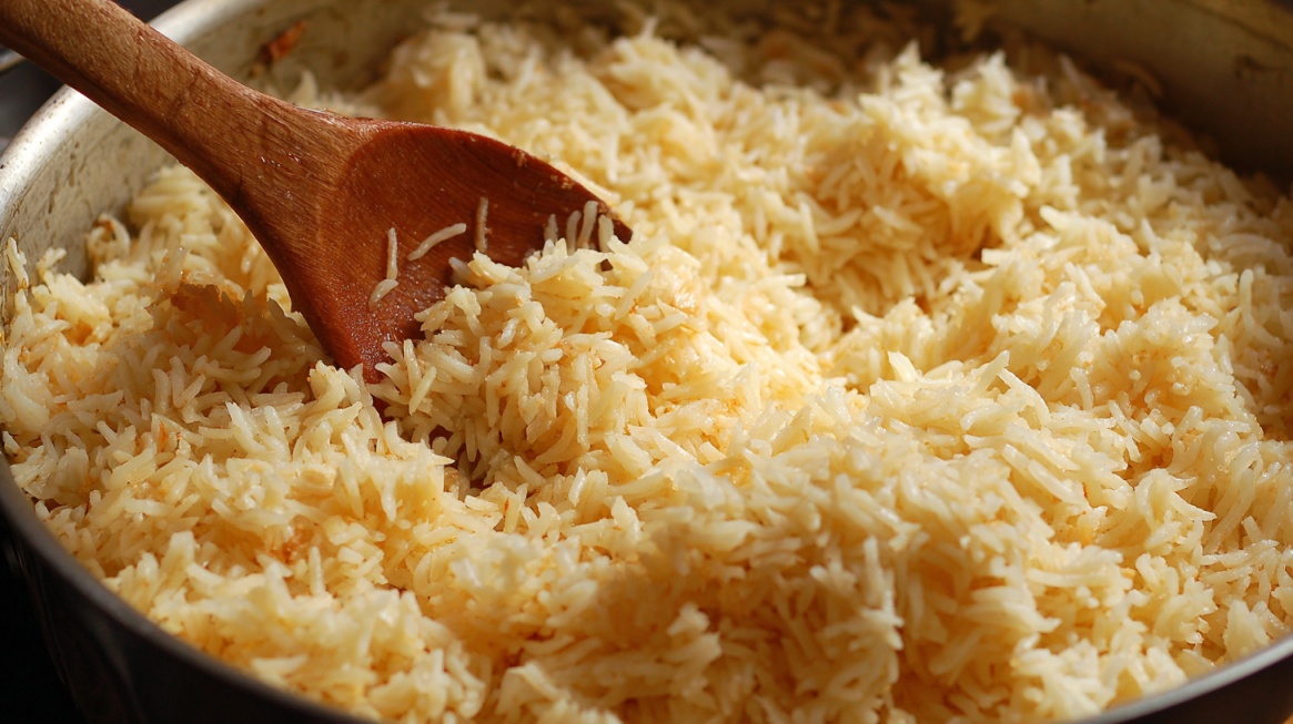 Cooked white rice in a pot with a wooden spoon mixing it