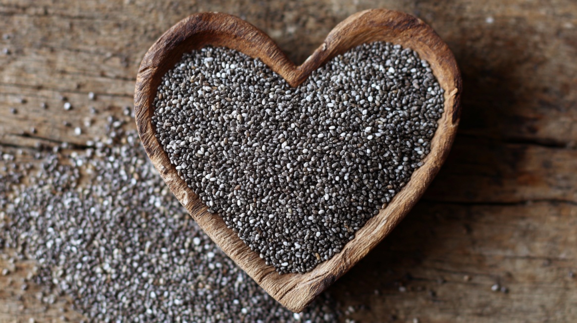 Heart-shaped wooden bowl filled with chia seeds on a rustic surface