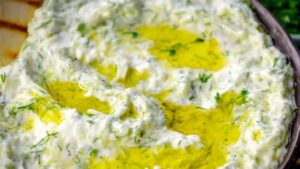 A close-up of creamy tzatziki sauce topped with olive oil and fresh herbs ready to serve