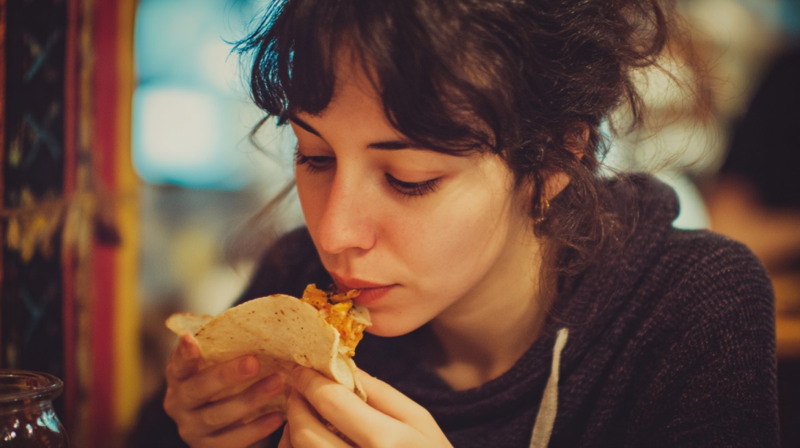 A person eating a tortilla, taking a bite while holding it close
