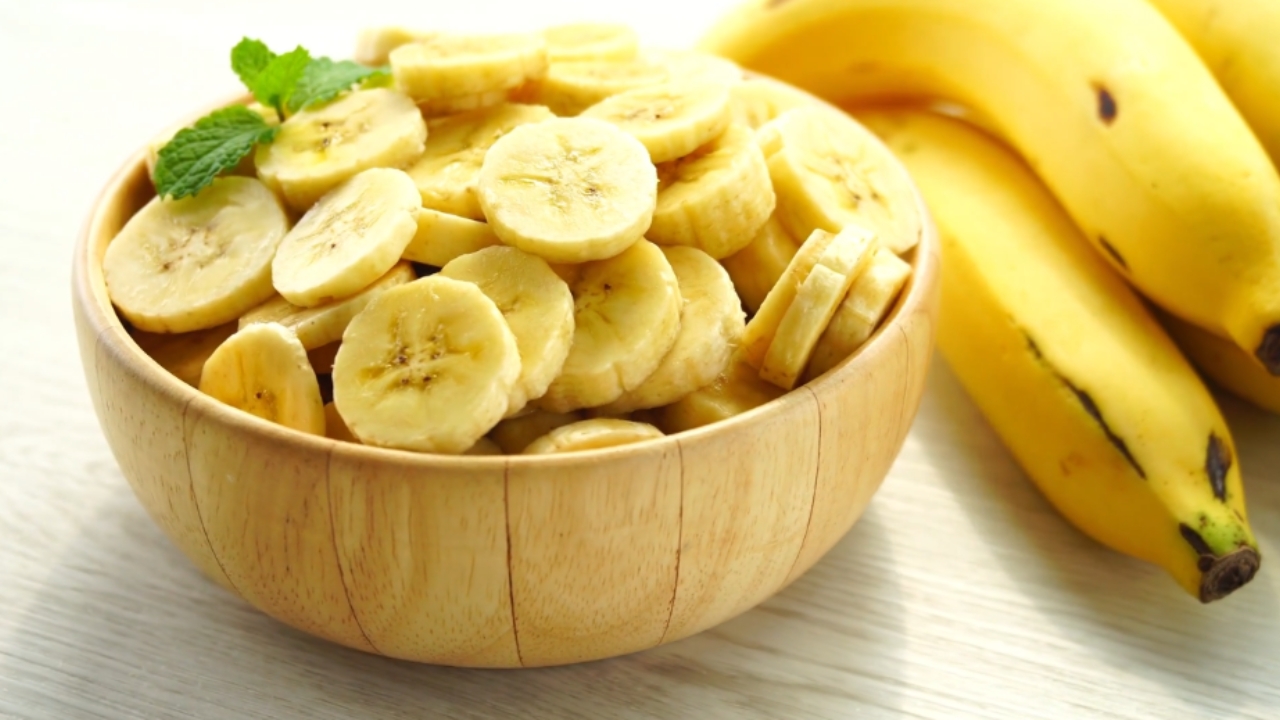 Kriške banane u drvenoj činiji uz cele zrele banane na stolu