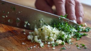 Hand chopping garlic and fresh parsley on a wooden cutting board
