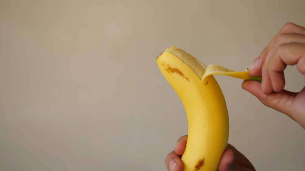 Ruka ljušti zrelu bananu dok se žuta kora polako odvaja