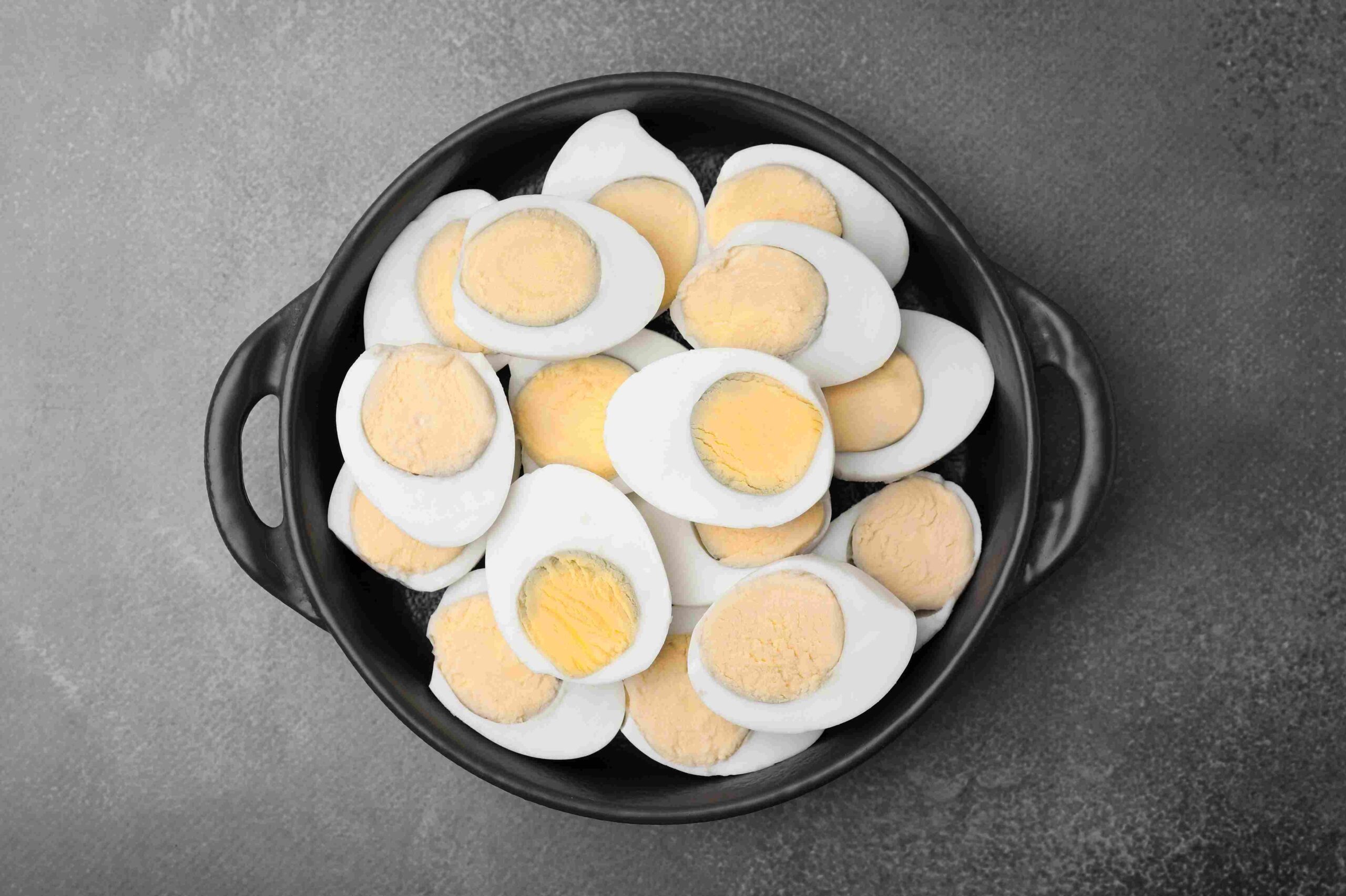 Bowl filled with sliced hard boiled eggs on a gray surface