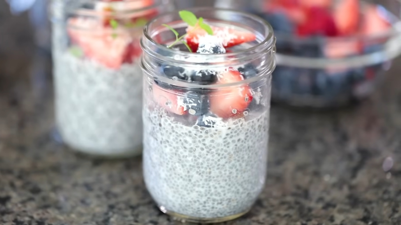A jar of chia seed pudding topped with fresh strawberries and blueberries on a kitchen countertop