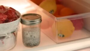 A jar of chia seed pudding chilling in a refrigerator next to fresh fruit