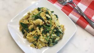 Scrambled eggs with spinach and onions served on a white plate with red pepper flakes on top