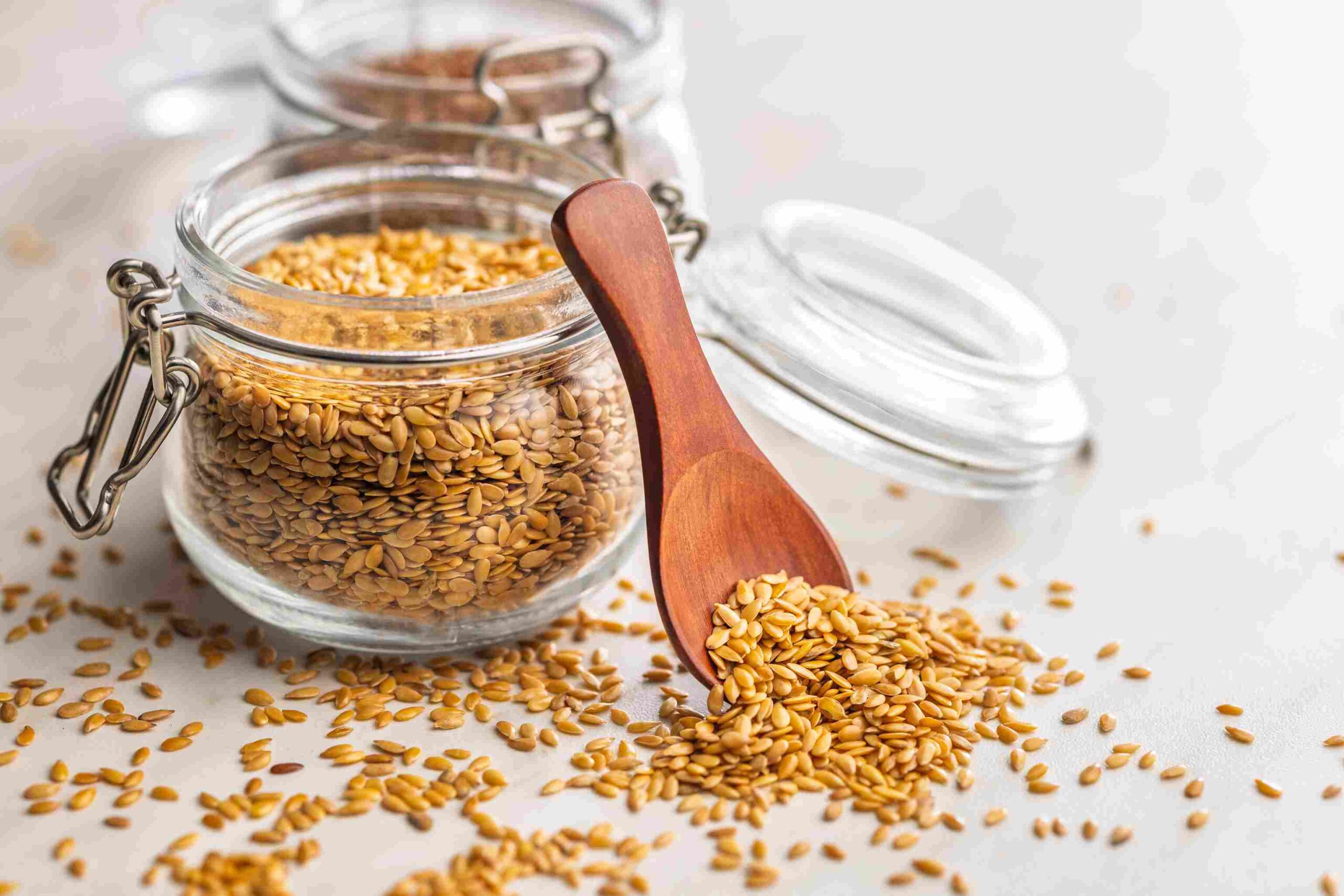 Flaxseeds in a glass jar with a wooden spoon spilling seeds onto a surface