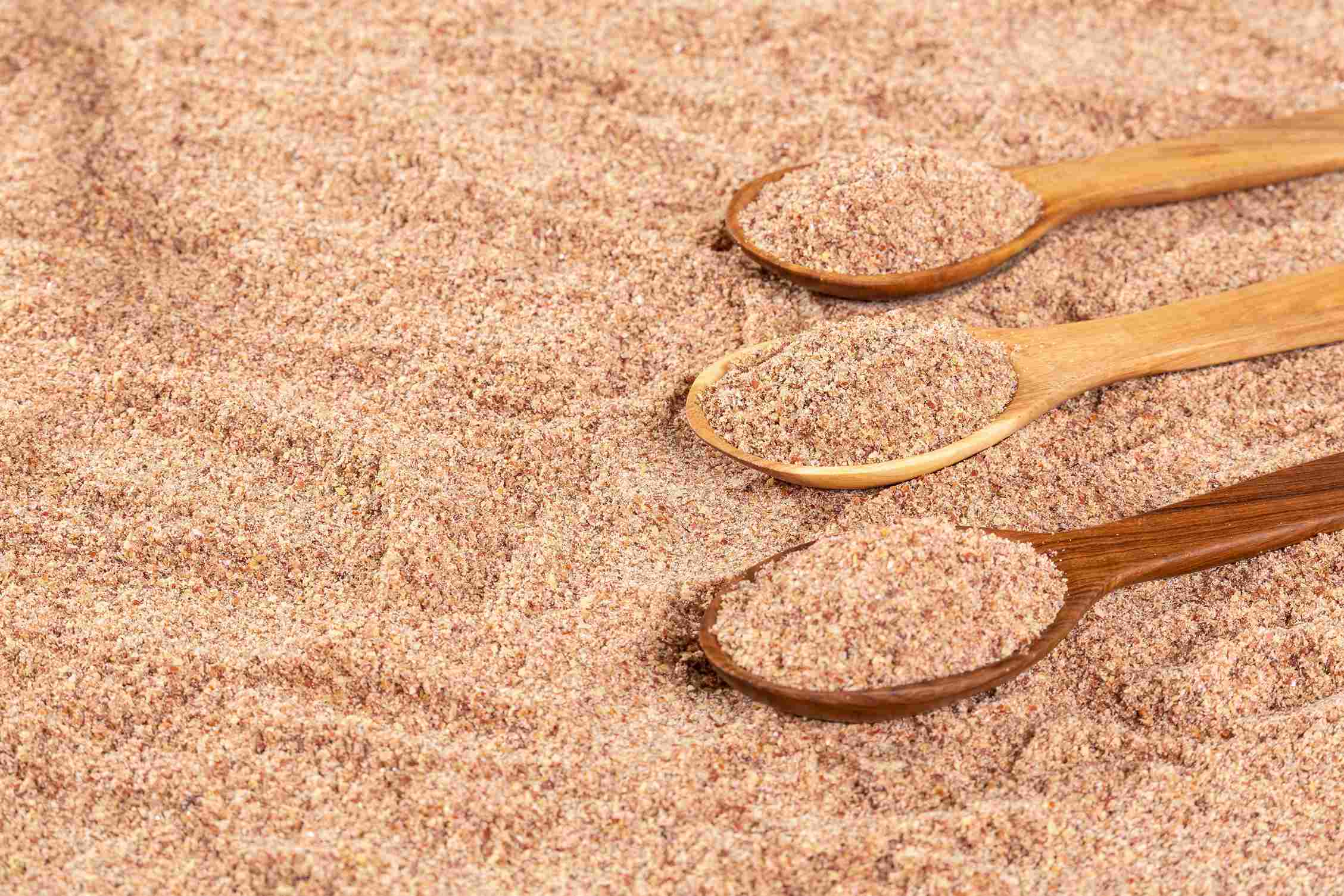 Ground flaxseed meal with wooden spoons scooping the powder