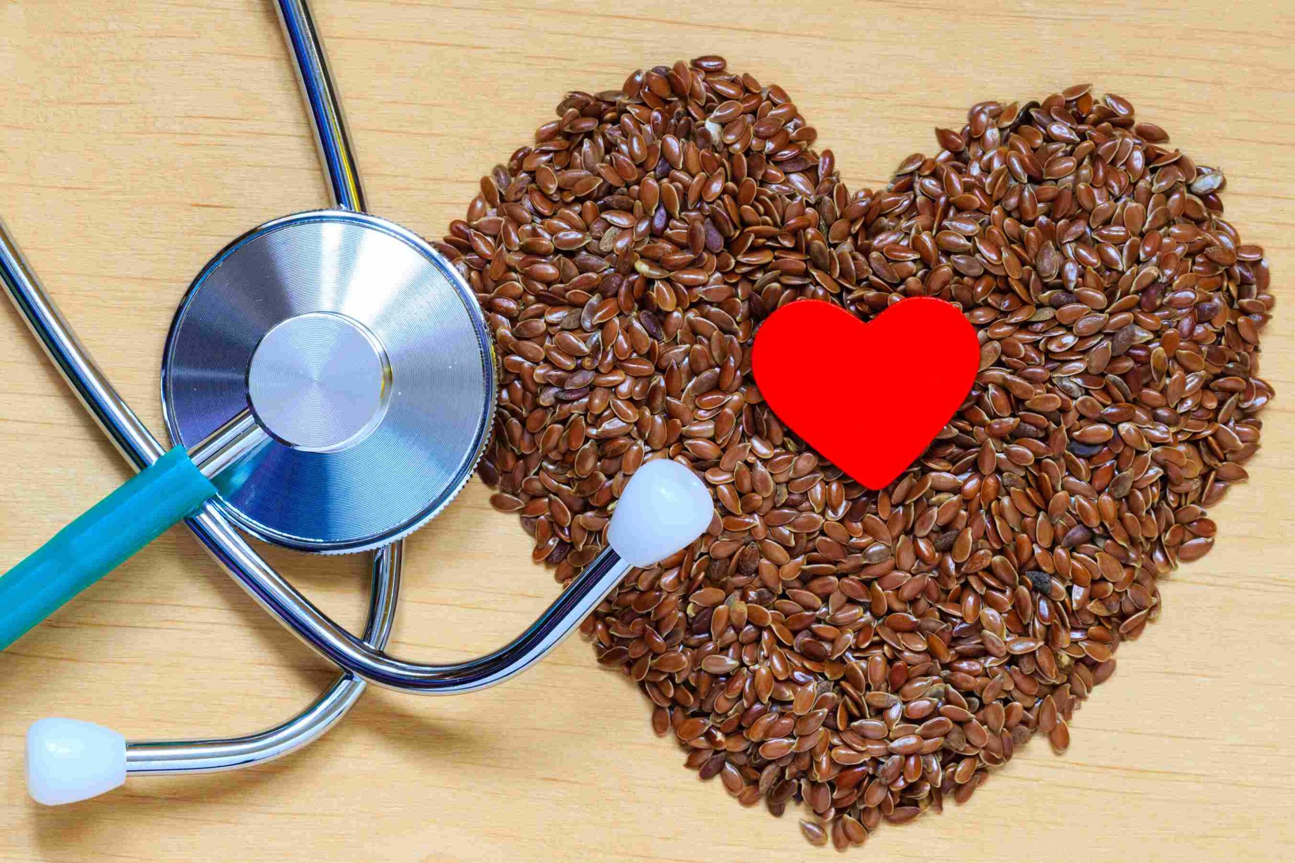 Flaxseeds arranged in a heart shape beside a stethoscope on a wooden surface