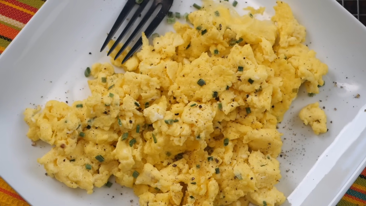 A plate of soft scrambled eggs topped with chives and black pepper with a fork on the side