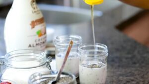 Honey being poured into jars of chia pudding with almond milk and chia seeds on a kitchen counter