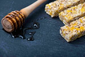 No-bake oat bars cut into squares with honey dipper and drizzle on a dark surface