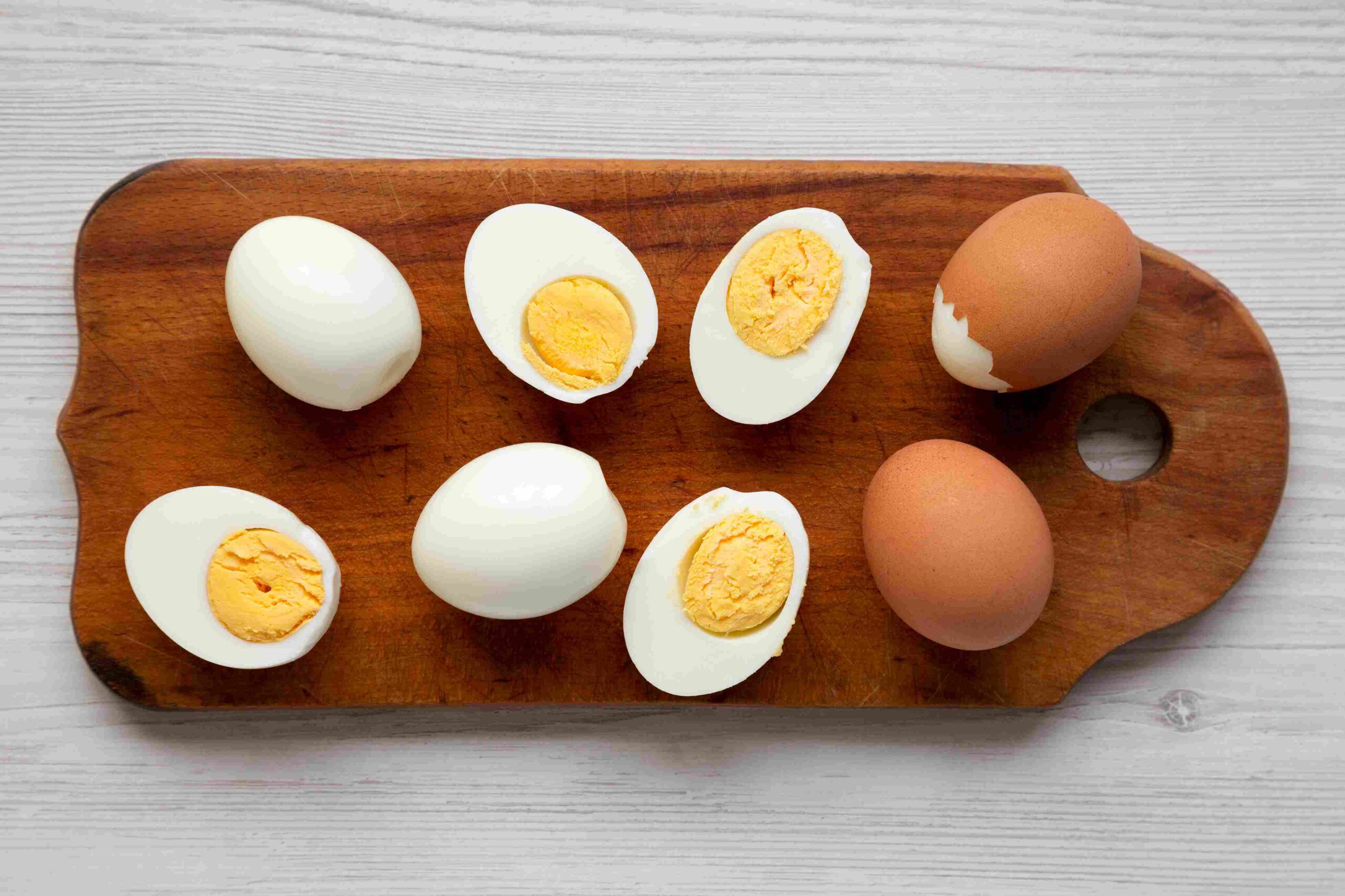 Boiled eggs, both whole and sliced, arranged on a wooden cutting board