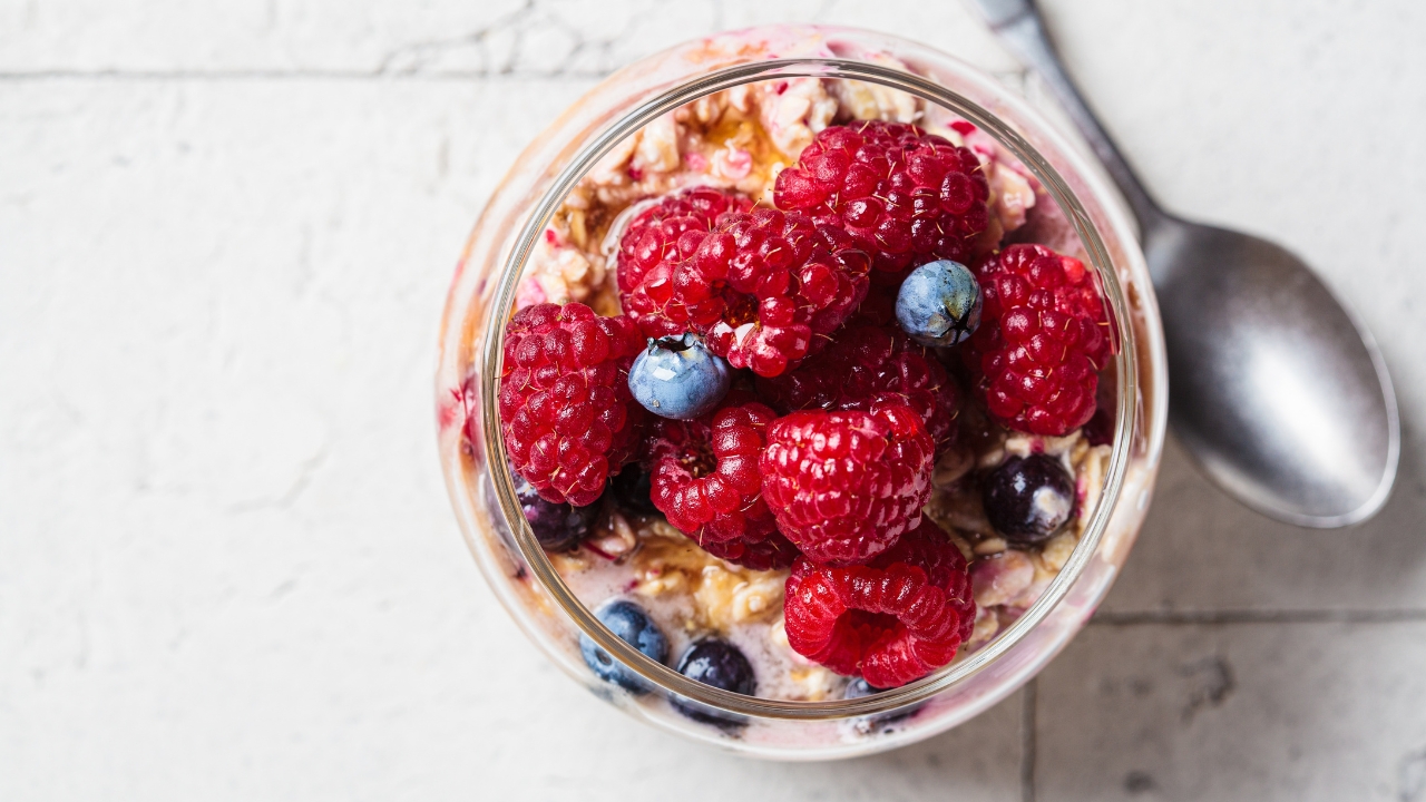 A jar of creamy overnight oats topped with fresh raspberries and blueberries
