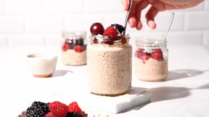 A spoon scooping creamy overnight oats topped with berries from a jar