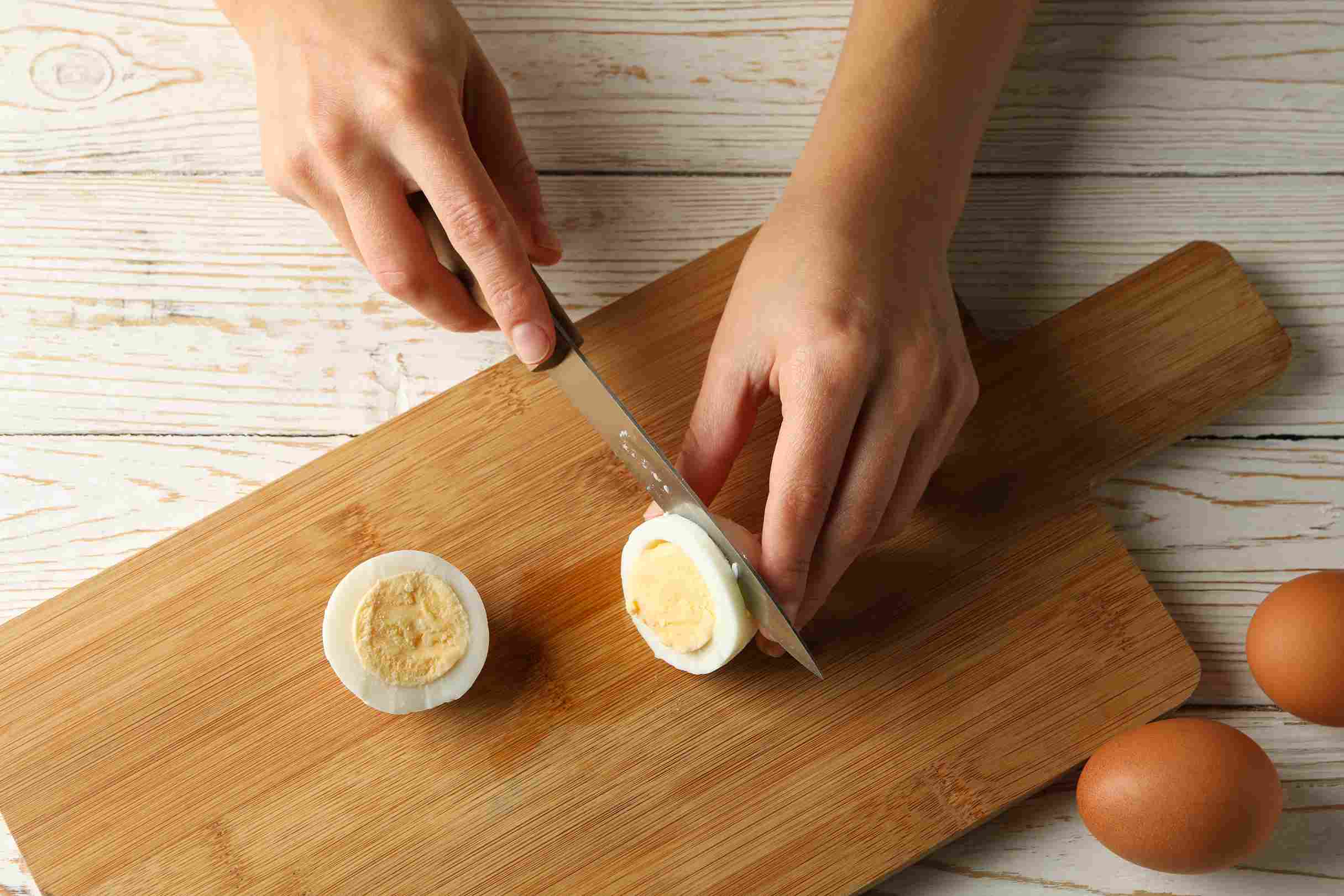 Hands cutting a boiled egg on a wooden cutting board