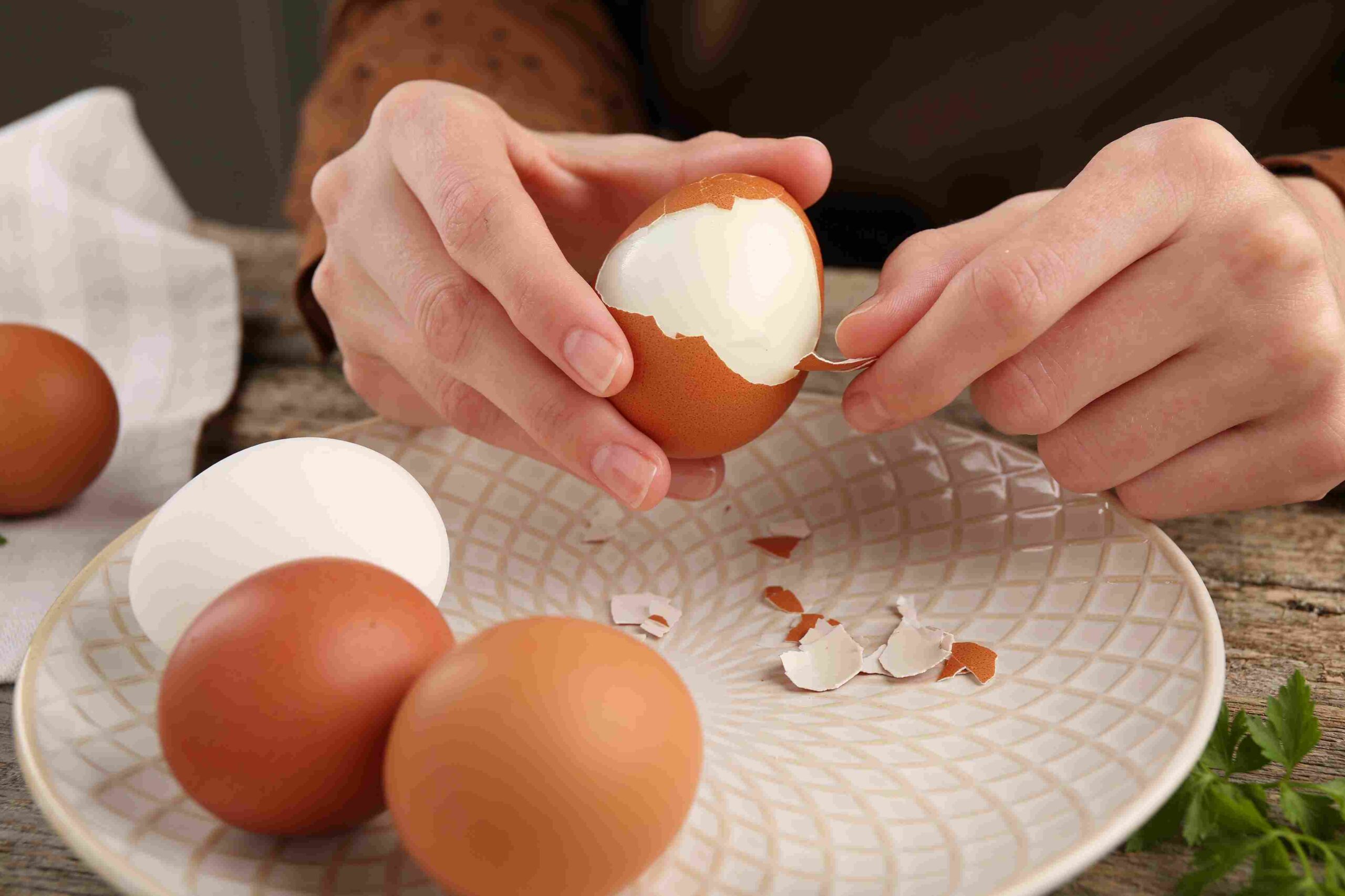 Hands removing the shell from a boiled egg over a plate with other eggs