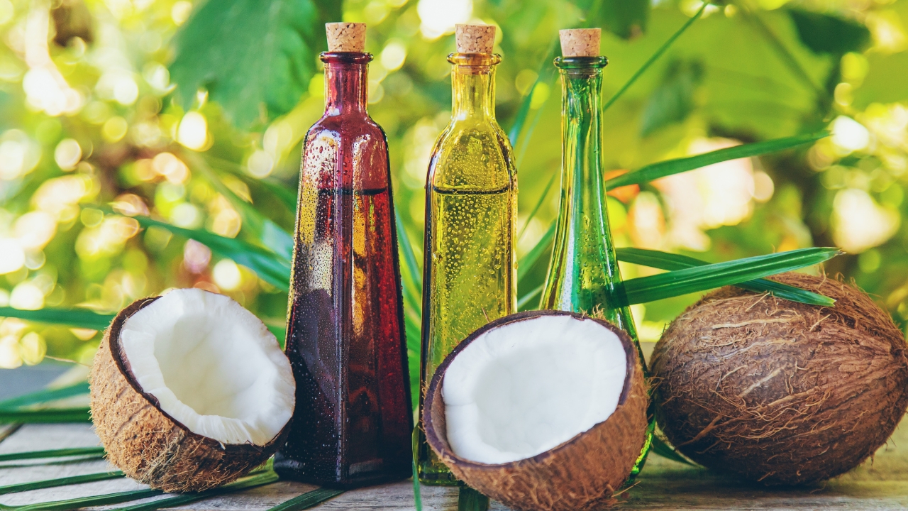 Coconut halves sit beside glass bottles of cooking oil on a green outdoor table