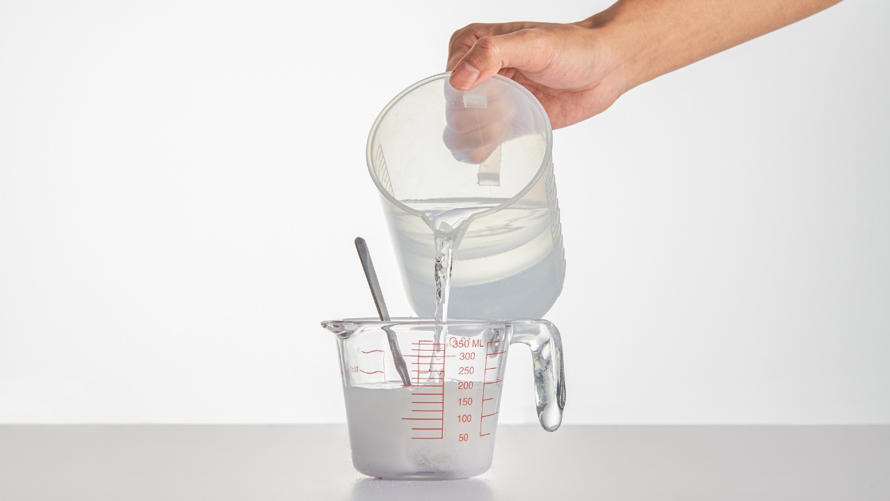 Water pours from one measuring jug into another with red volume marks