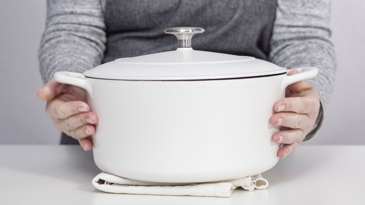 A person holds a white Dutch oven with a lid on a kitchen counter