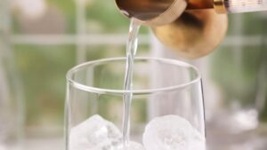 Fresh lime juice being poured over ice in a glass for dirty soda.