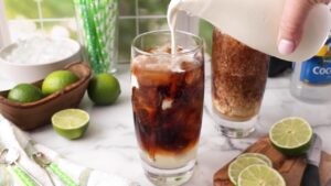 Cream being poured into a glass of cola dirty soda with ice and lime