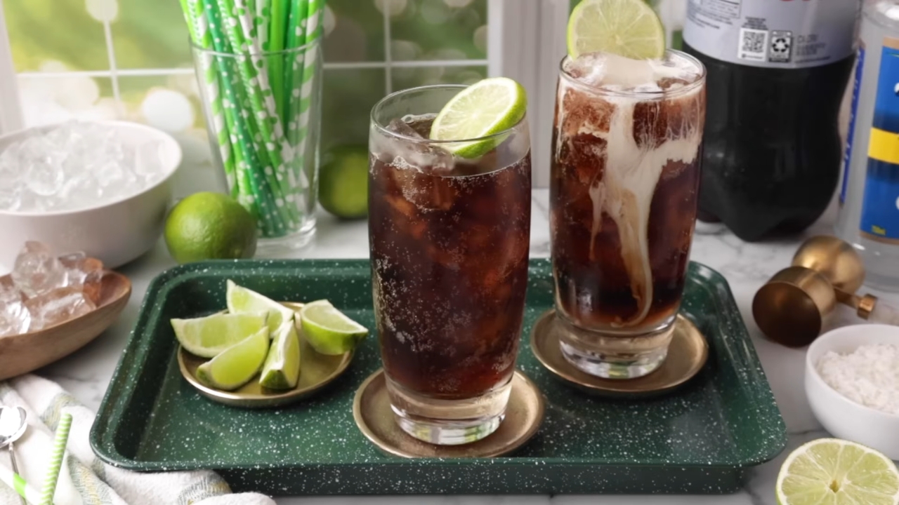 Two glasses of cola dirty soda with cream, ice, and fresh lime wedges