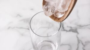 Ice cubes being poured into a tall glass for dirty soda