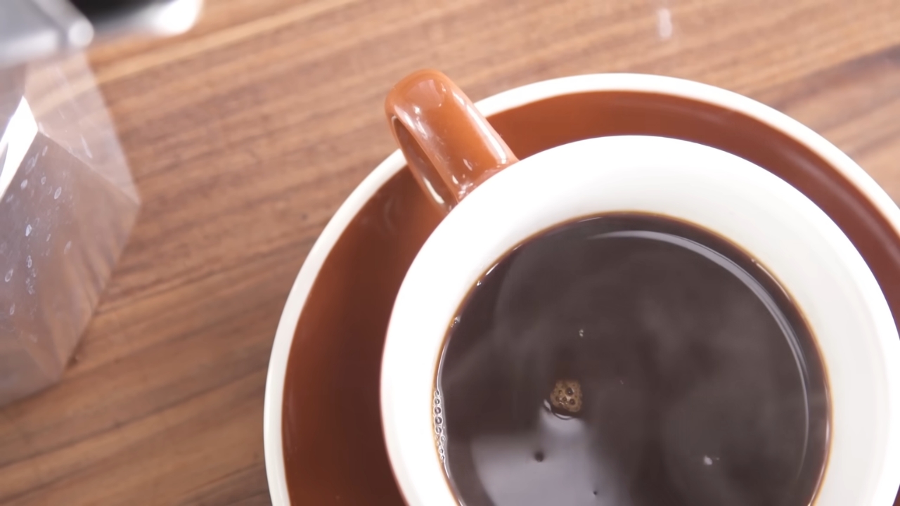Cup of strong black coffee beside a Moka pot on a wooden table