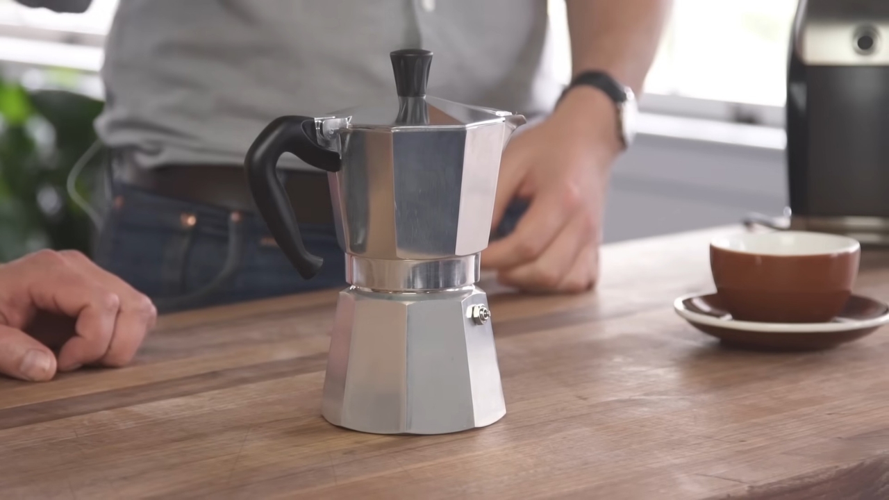 Moka pot on a kitchen counter beside a coffee cup