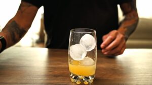 Orange juice and ice cubes in a tall glass on a wooden table