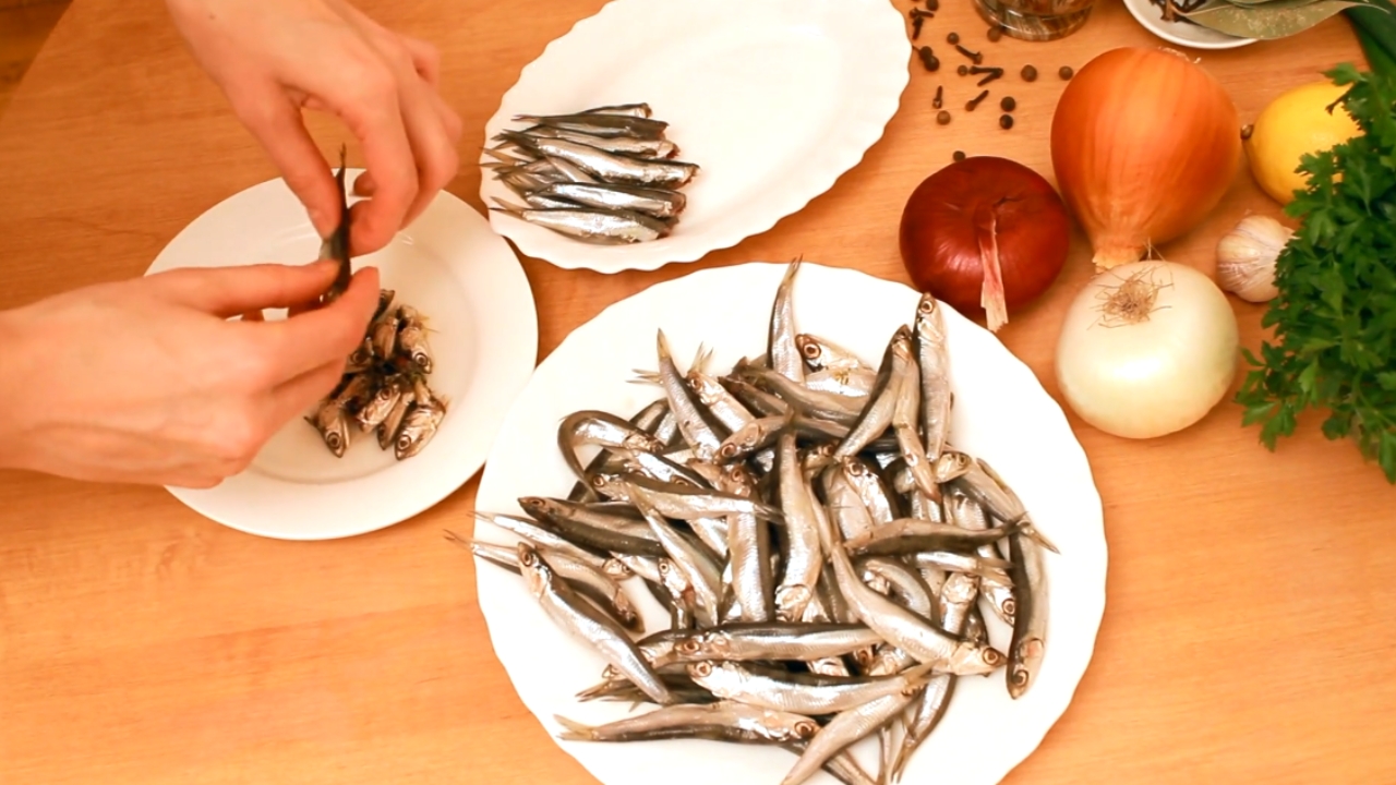Fresh anchovies sit on plates beside onions, garlic, lemon, and parsley.