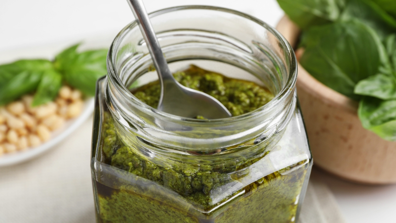 Jar of green pesto with basil leaves and pine nuts.