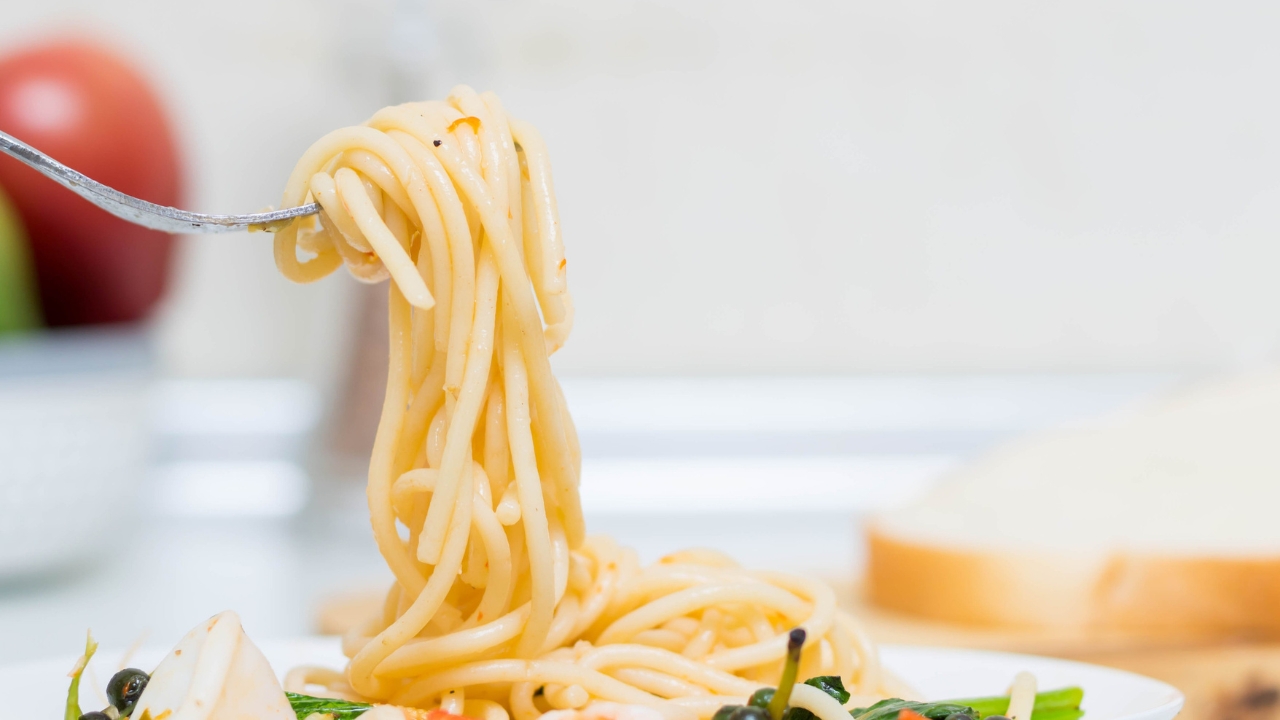 A fork lifts cooked spaghetti above a plate.