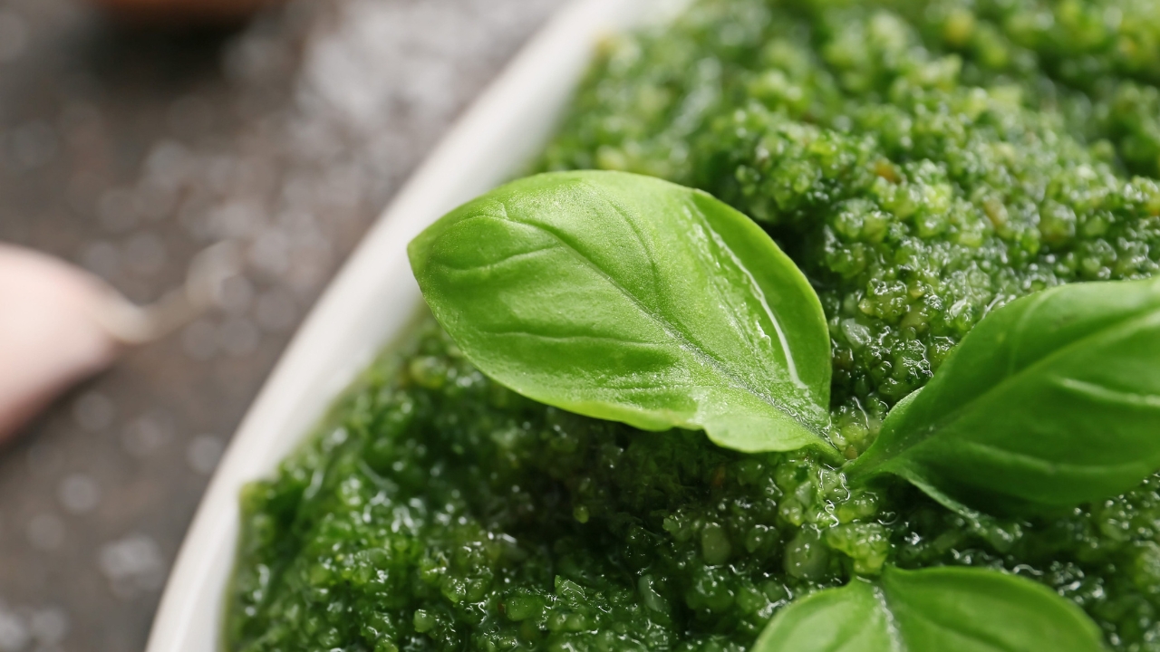 Fresh basil leaves on a bowl of green pesto sauce.