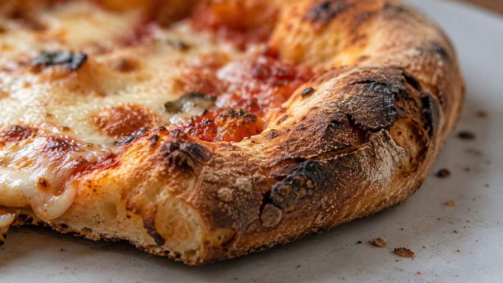 Extreme close-up of a pizza crust with a dry, heavily browned surface, charred spots, and melted cheese.